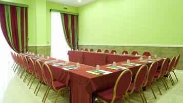 Un salón de conferencias con varias mesas y sillas, paredes verdes y cortinas.