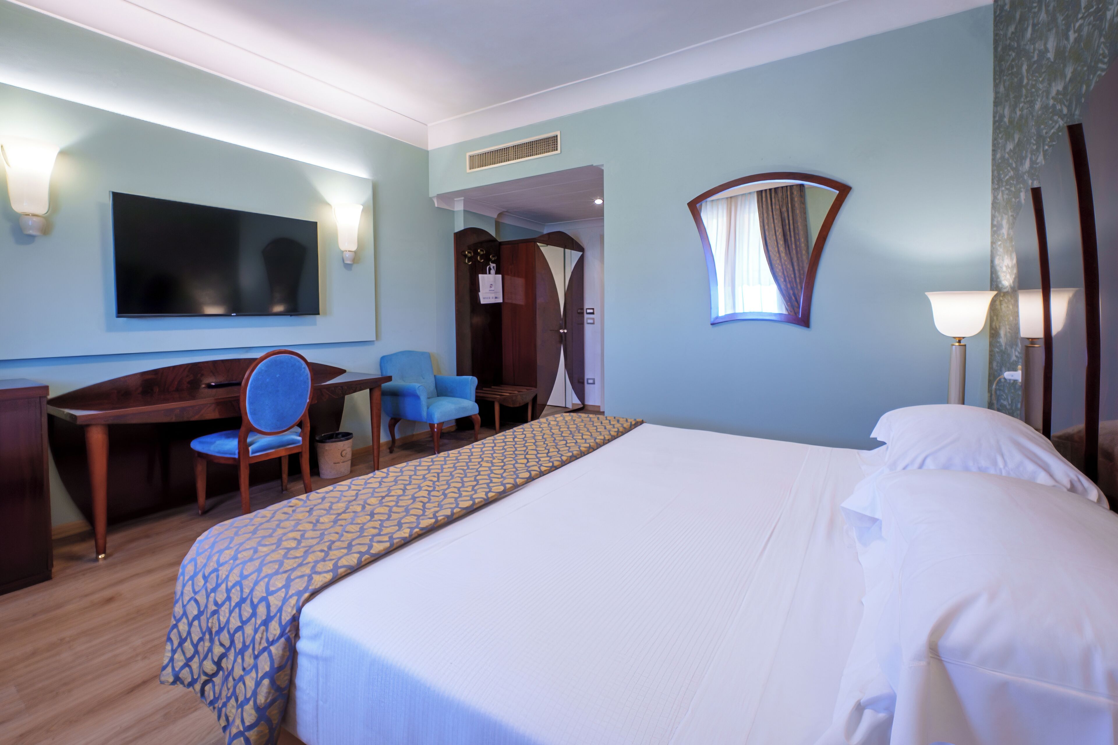 Une chambre d’hôtel équipée d’un lit, d’un bureau, d’une chaise, d’une télévision et d’une fenêtre avec des rideaux.