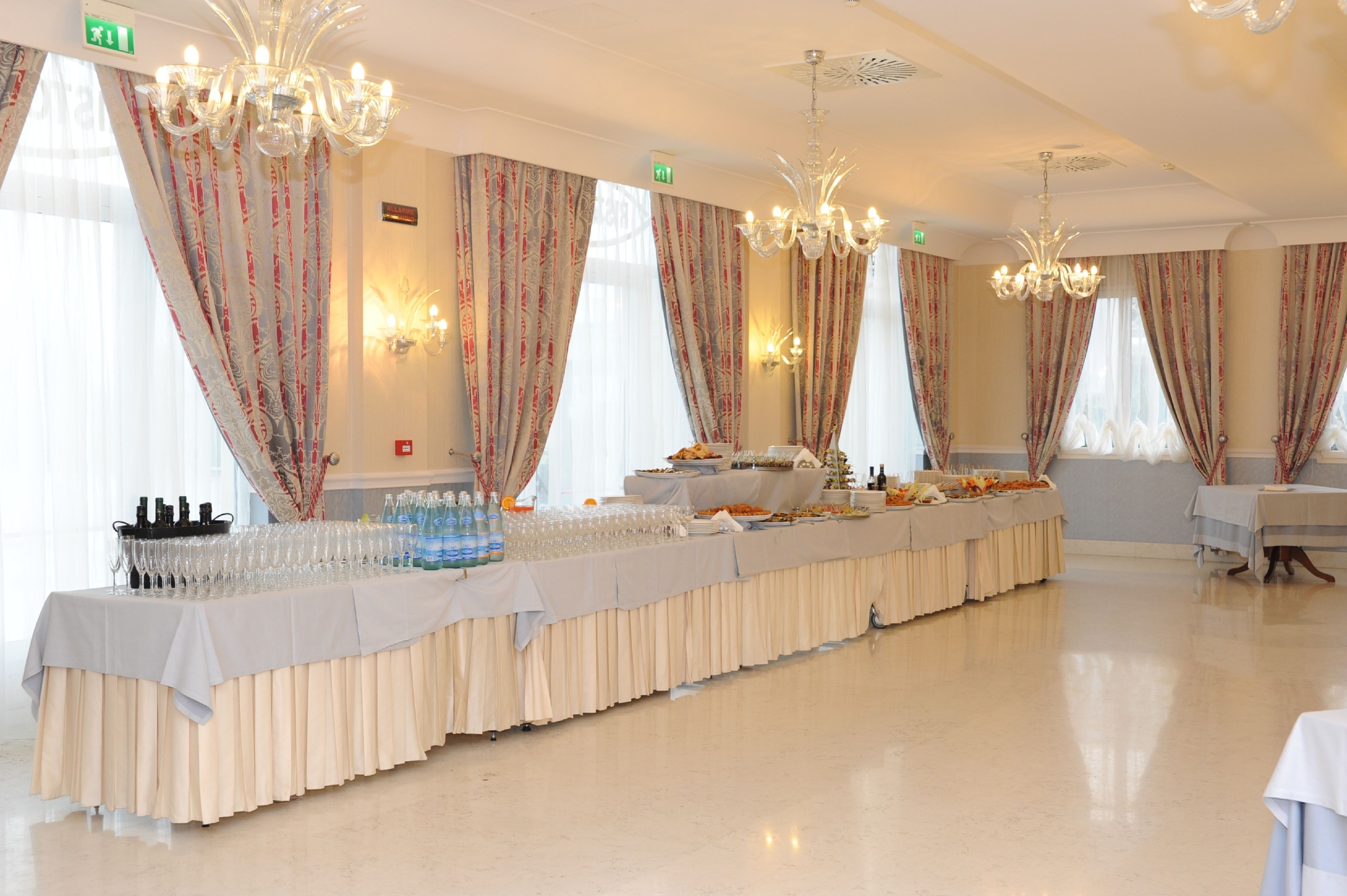 Un salón de banquetes con una larga mesa cubierta con mantel blanco, rodeado de cortinas florales y candelabros.