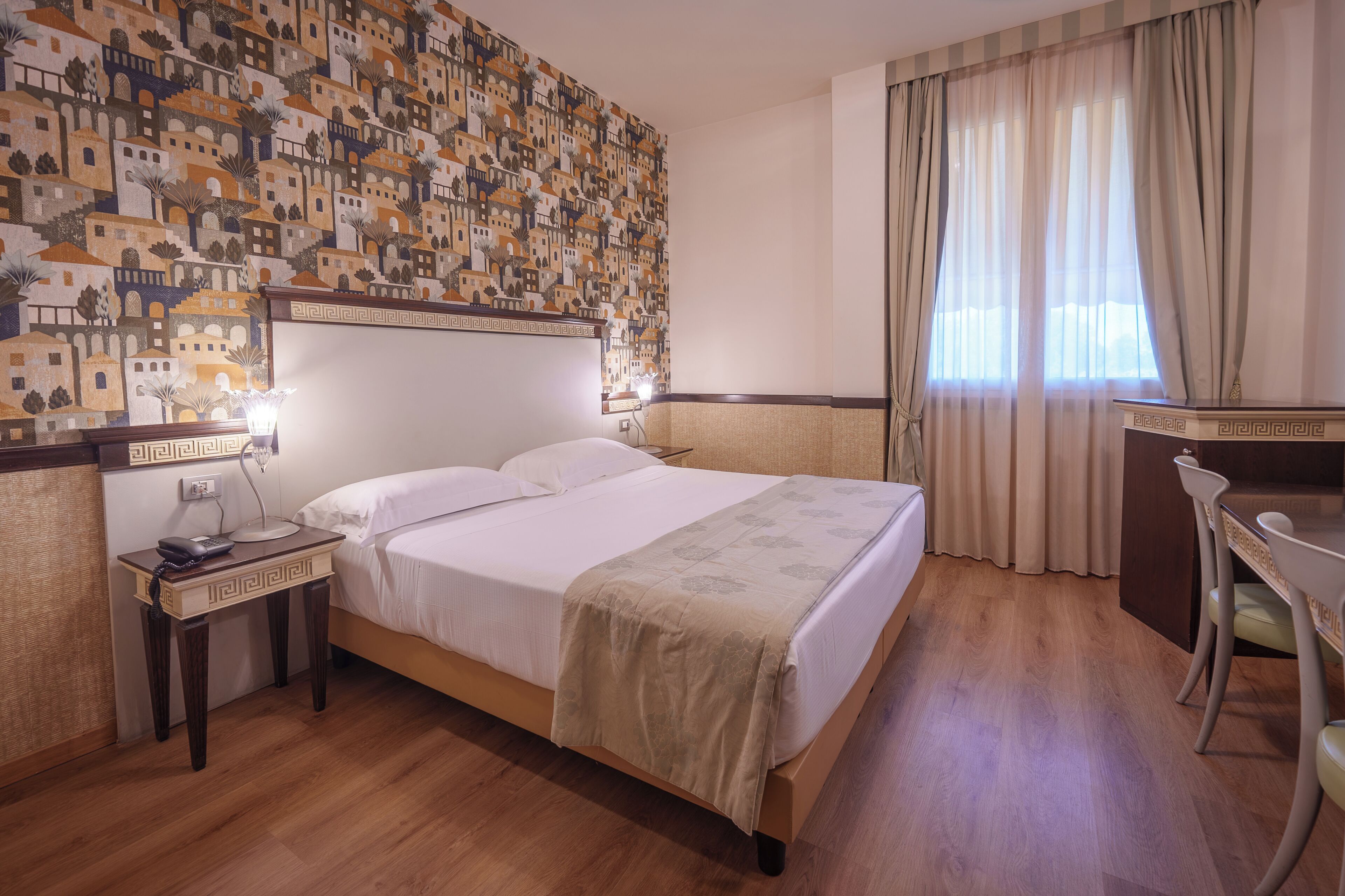 Habitación de hotel con cama, mesita de noche, lámpara, escritorio, silla y pared con diseño.