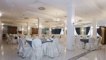Un salón de banquetes con varias mesas redondas, sillas blancas, candelabros y un suelo pulido.