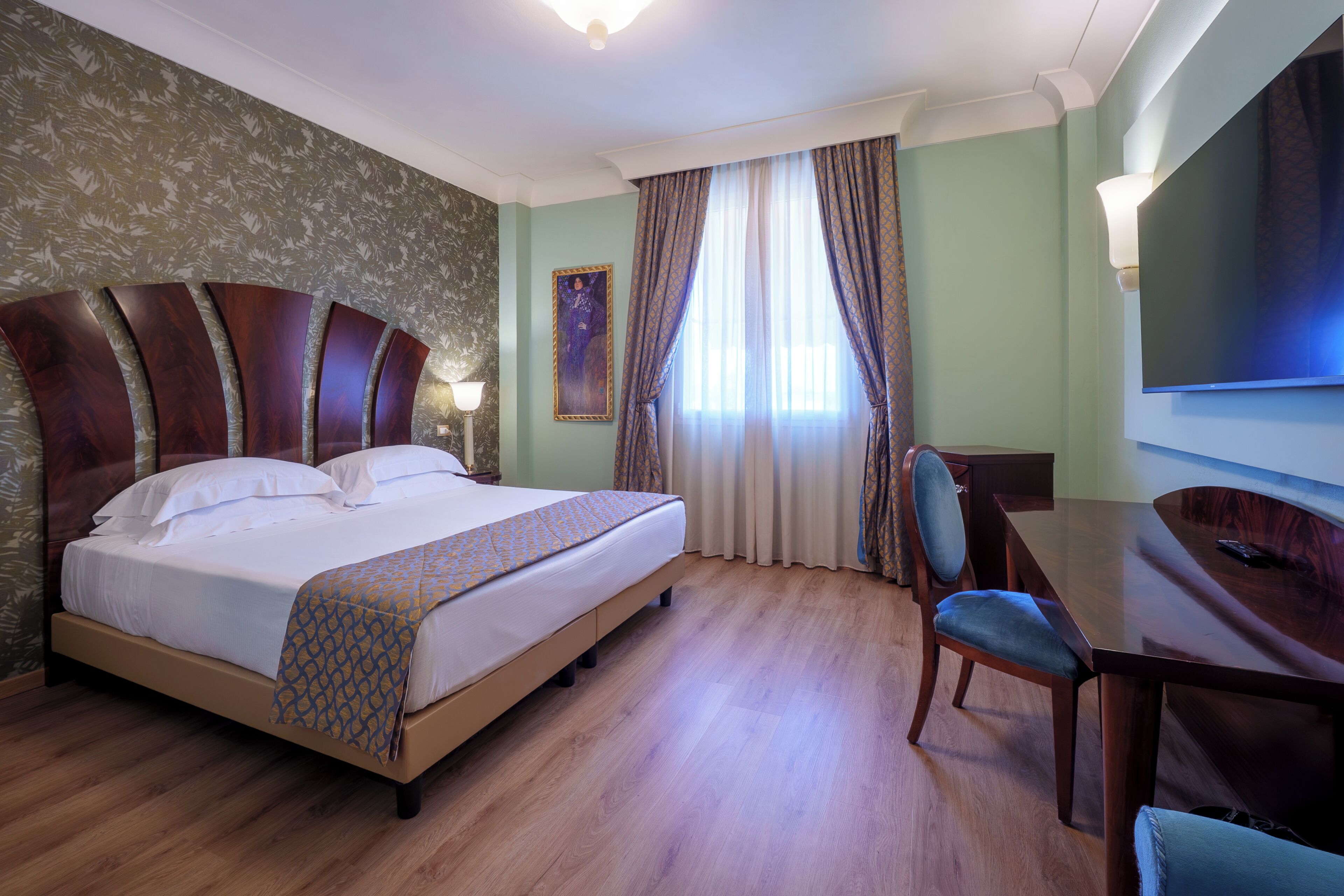 Habitación de hotel con una cama grande, un escritorio, una silla, un televisor y un cuadro en la pared.