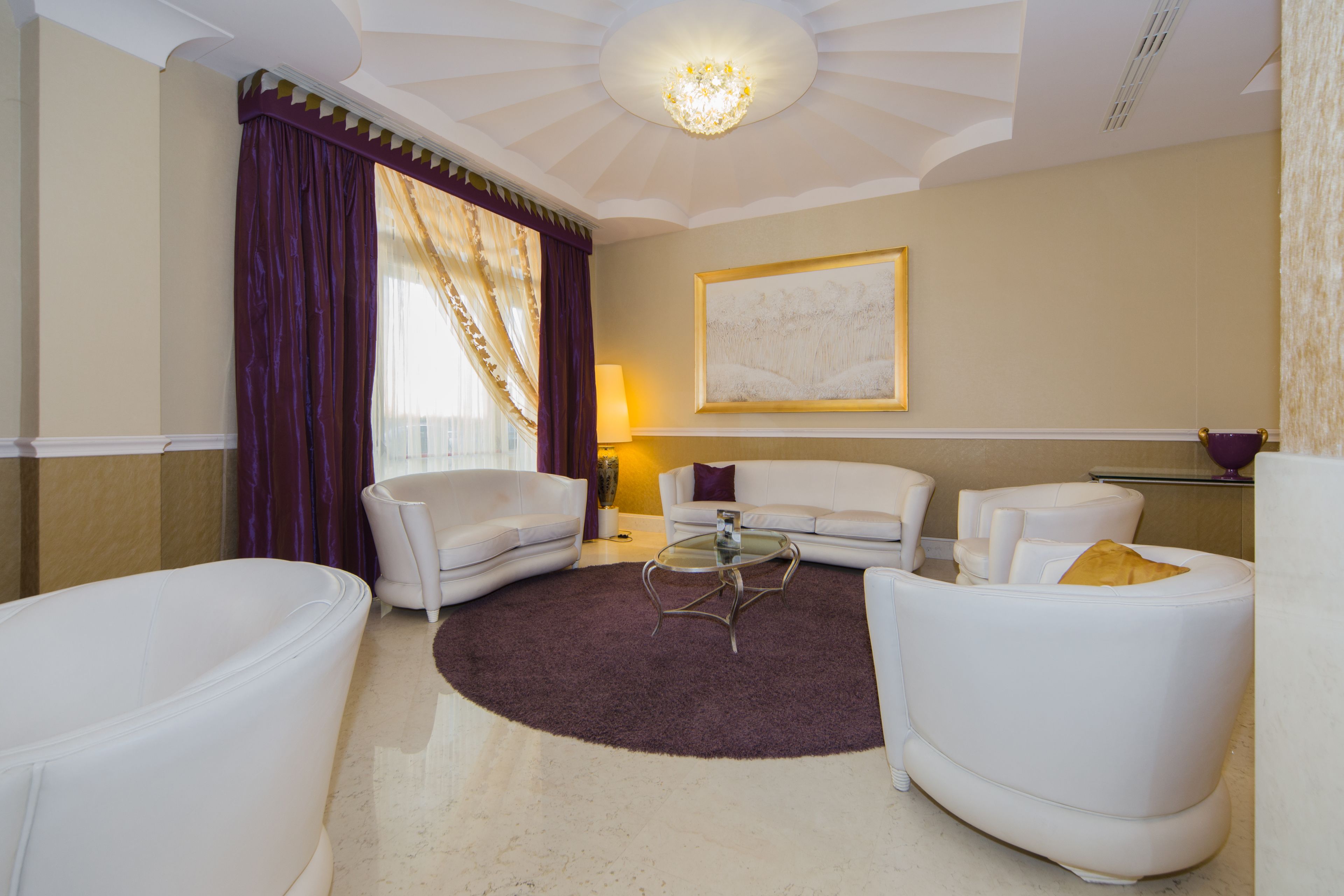 A modern living room with a round glass coffee table, white sofas, and a large abstract painting on the wall.