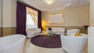 A modern living room with a round glass coffee table, white sofas, and a large abstract painting on the wall.