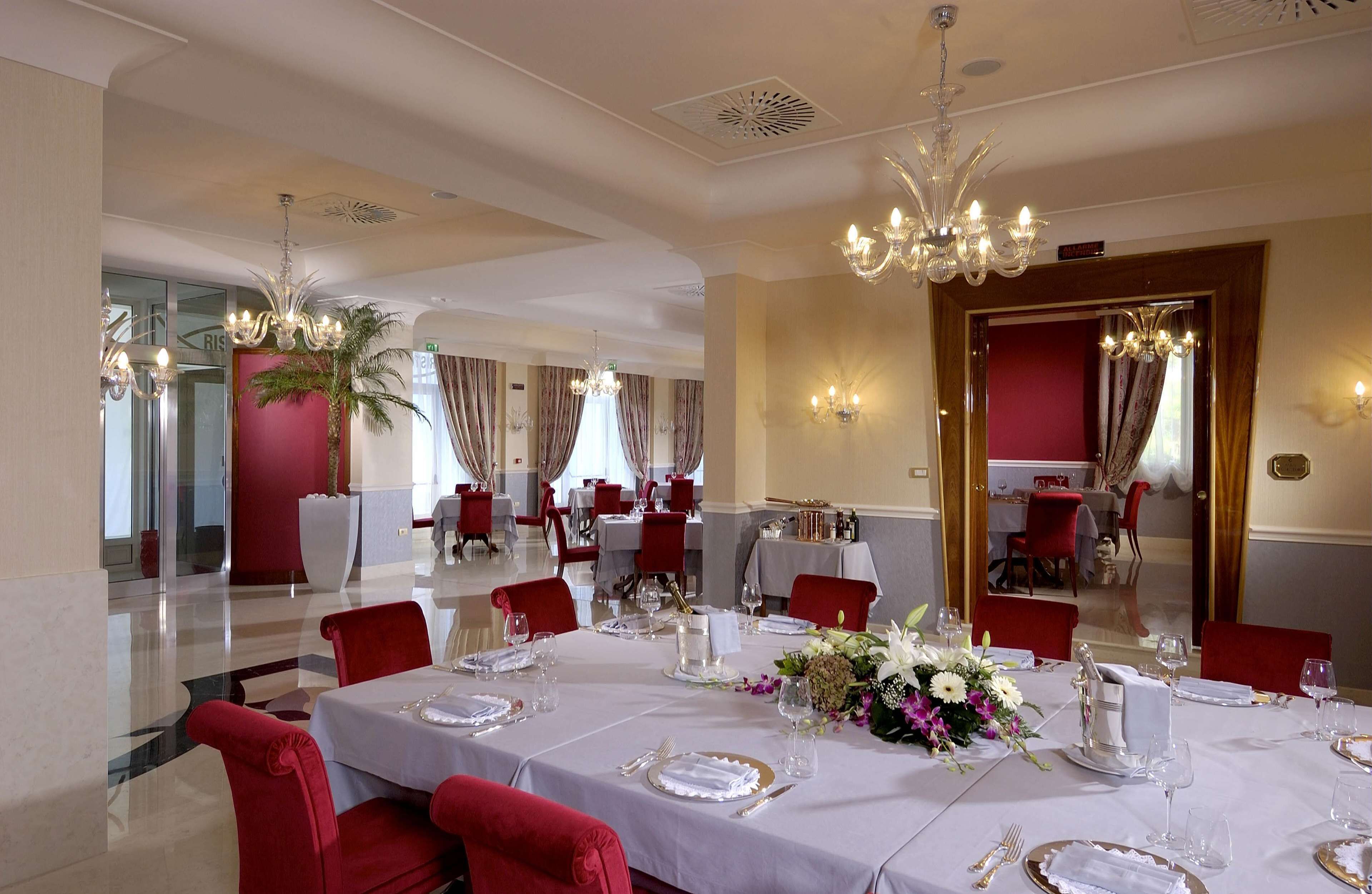 Un comedor con mesas dispuestas para una comida, sillas rojas, candelabros y una pared decorada en rojo.