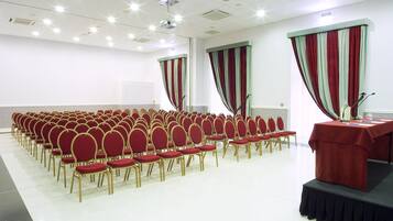 Uma sala de conferência com fileiras de cadeiras vermelhas e um palco com uma mesa vermelha.
