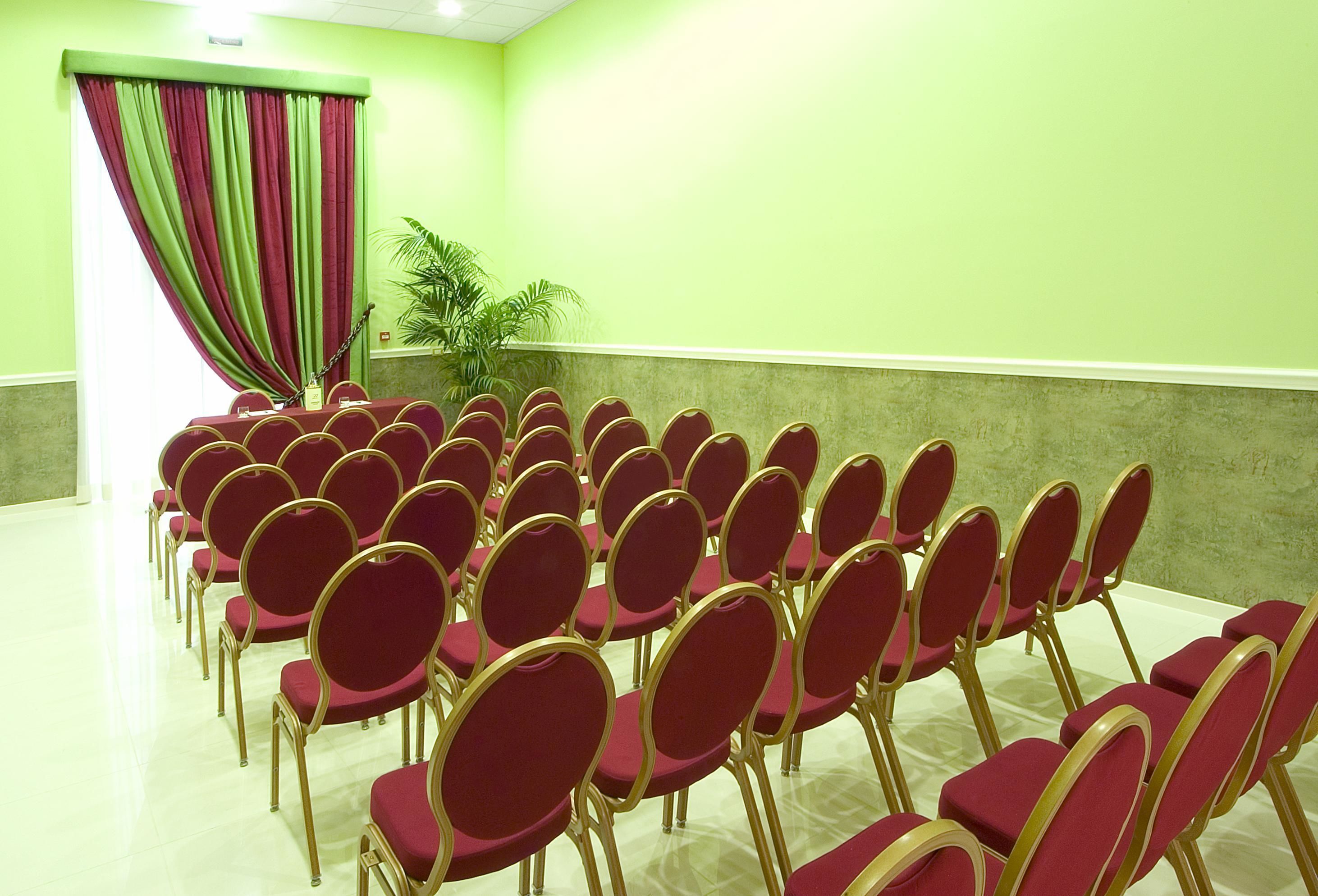 Uma sala de conferências com fileiras de cadeiras vermelhas e uma cortina verde.