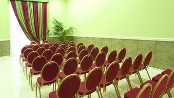 Uma sala de conferências com fileiras de cadeiras vermelhas e uma cortina verde.