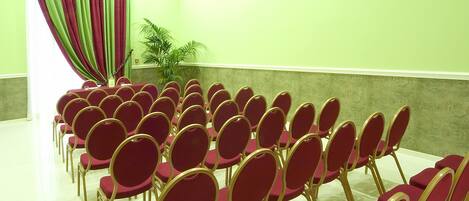 Un salón de conferencias con hileras de sillas rojas y una cortina verde.