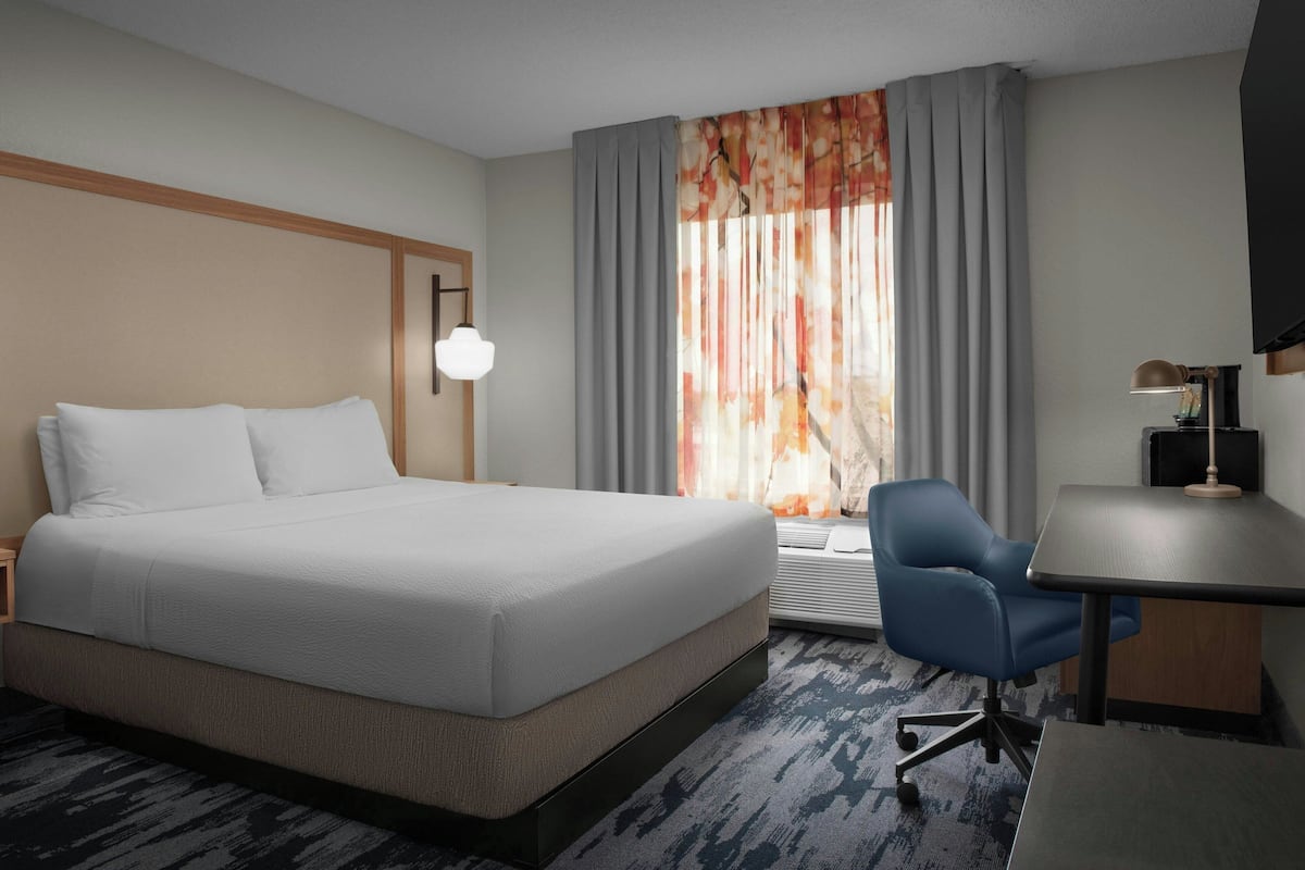 A hotel room with a large bed, a desk, a chair, and a window with curtains.