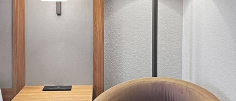 A modern room with a wooden nightstand, a lamp, and a cushioned chair.