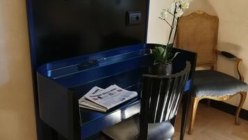 Una habitación con un escritorio azul, una silla negra, un televisor, un cuadro enmarco y una orquídea en maceta.