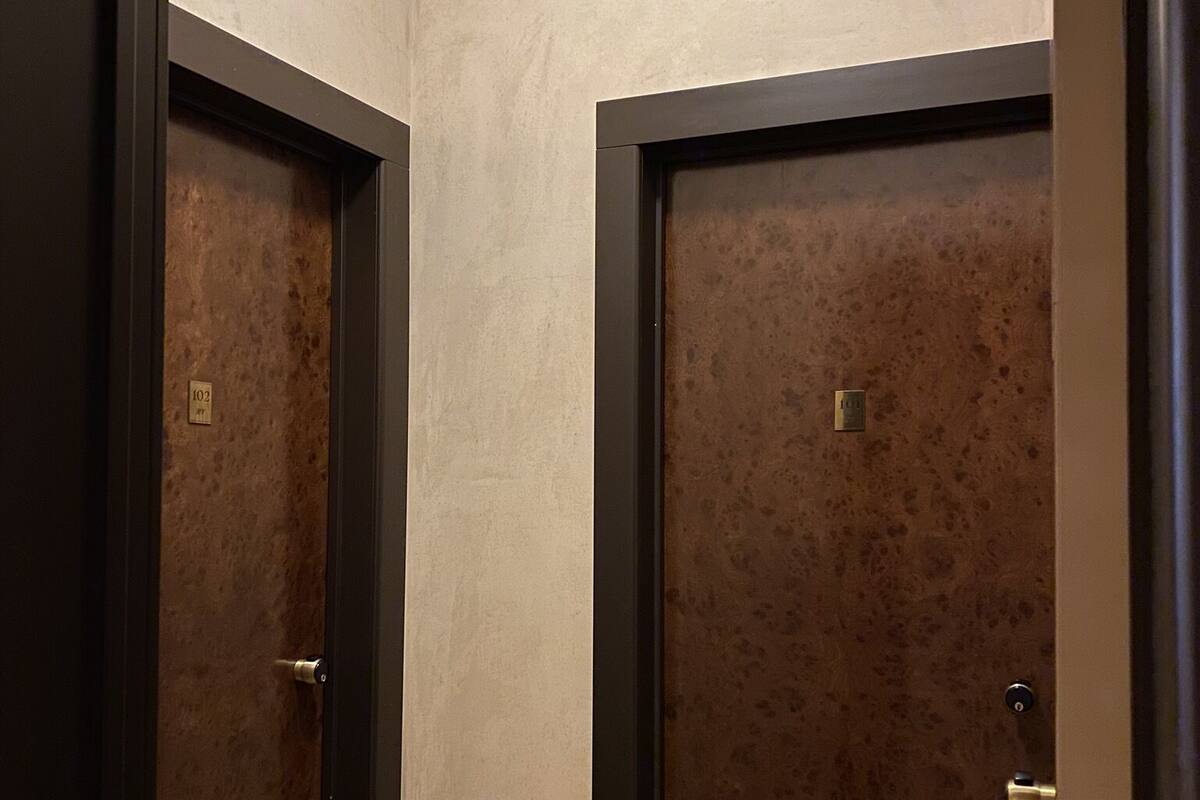 Un pasillo con dos puertas, cada una con una placa de identificación. Las paredes tienen una textura marcada y el suelo es de madera.