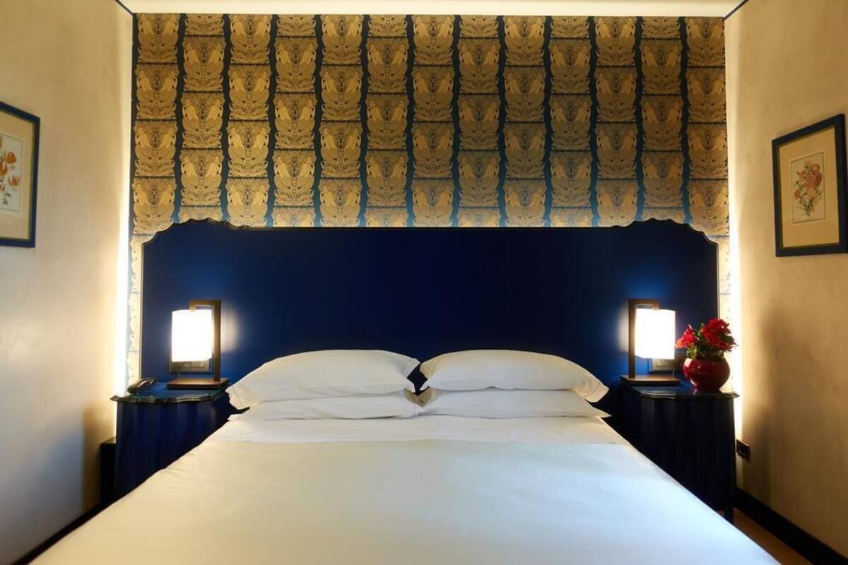 Una habitación de hotel con una cama grande, dos mesitas de noche con lámparas, un valance decorativo y cuadros enmarcados en las paredes.