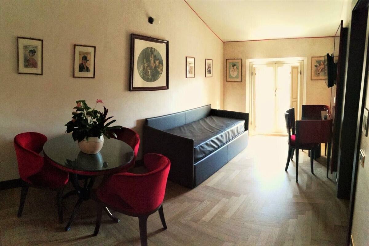Una sala moderna con una mesa redonda de comedor, sillas rojas, un sofá negro y una planta en maceta.
