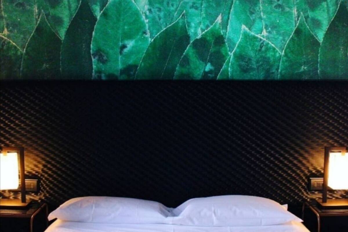 Una habitación de hotel con una cama, un cabecero con diseño de hojas y dos lámparas de noche.