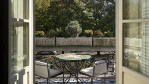 Une terrasse ouverte avec une table ronde et des chaises, un mur en pierre et des arbres en arrière-plan.