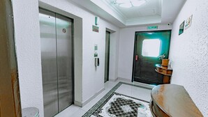 A hotel lobby with a central elevator, a reception desk, and a patterned rug on the floor. - Panorama Deira (Dubai)