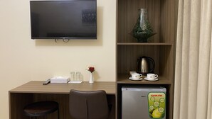 A hotel room with a wooden desk, a television, a refrigerator, a coffee maker, and a vase with a flower. - Panorama Deira (Dubai)