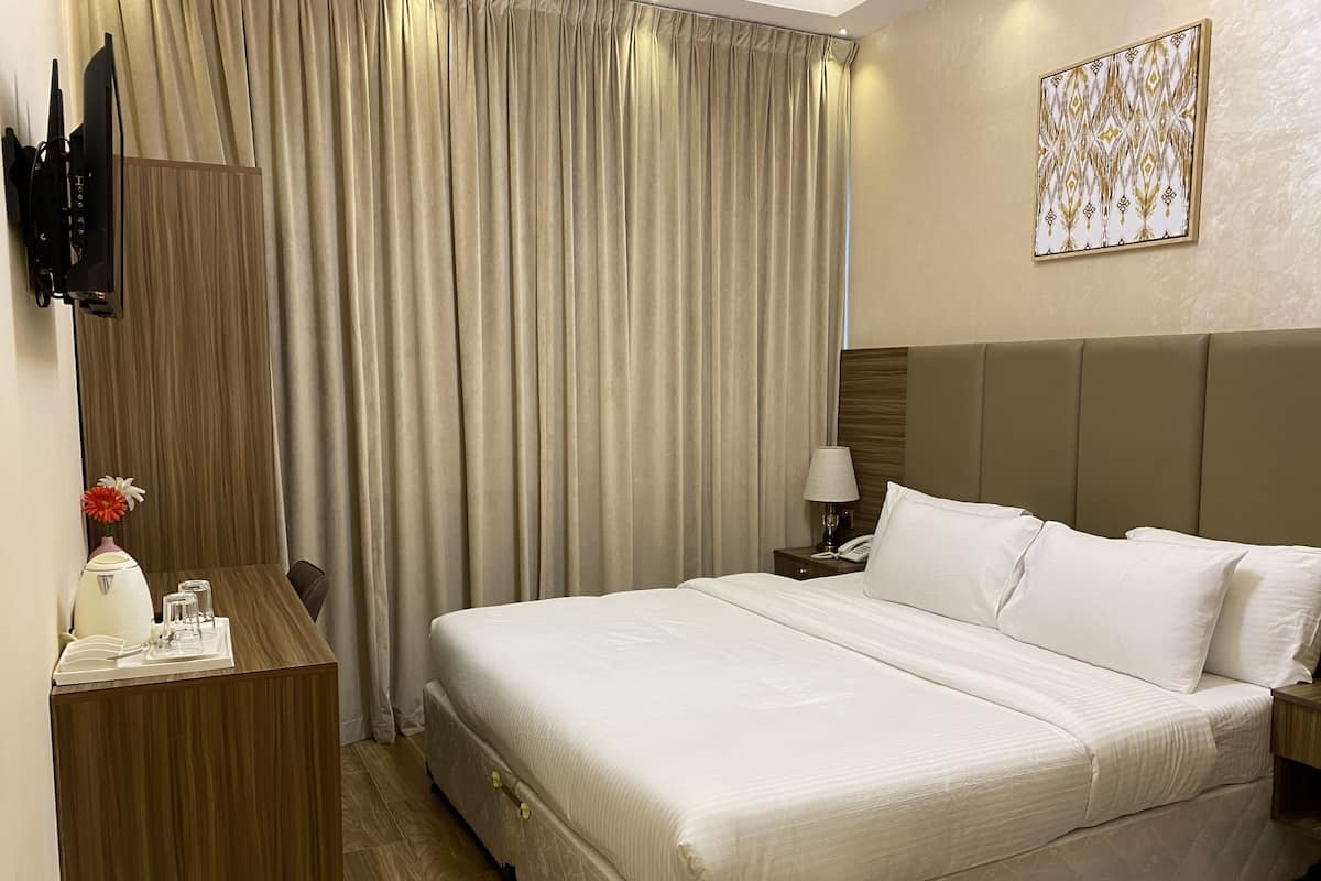 Une chambre d’hôtel avec un grand lit, un bureau avec une lampe, un téléviseur fixé au mur et un tableau accroché au mur.