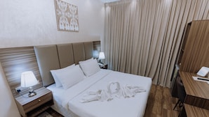 A hotel room with a large bed, a desk, a nightstand with a lamp, and a curtain. - Panorama Deira (Dubai)