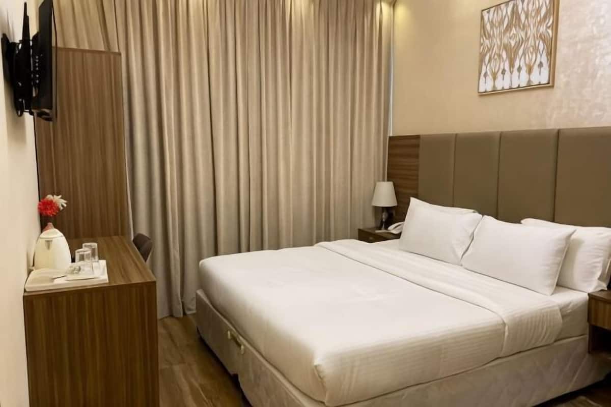 Une chambre d’hôtel avec un lit, un bureau, une lampe, une télévision et un rideau.