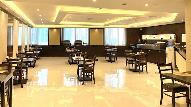 A hotel dining area with multiple tables and chairs, a bar, and large windows. - Panorama Deira (Dubai)