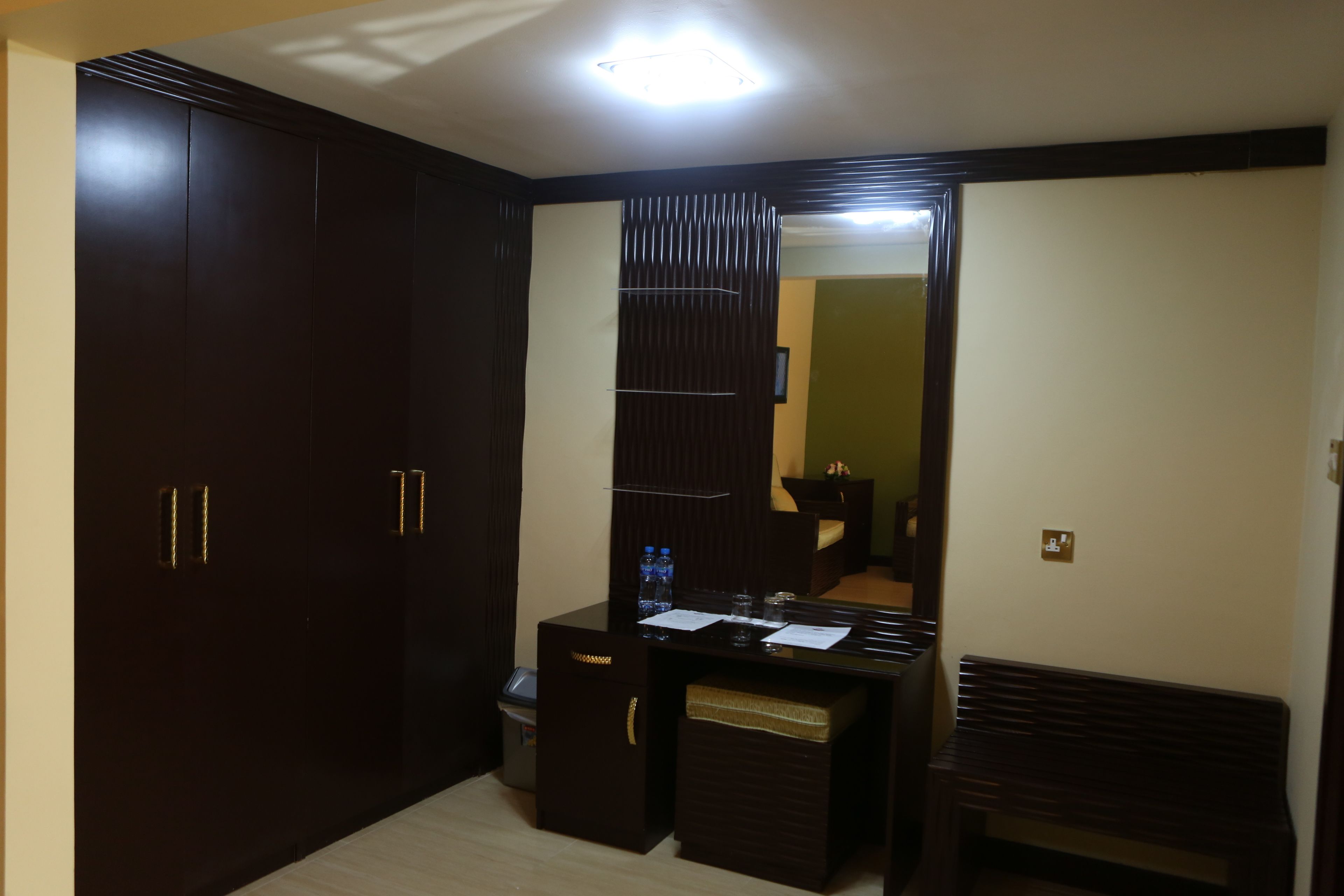 Una habitación con un armario de madera oscura, un escritorio con espejo y un banco.