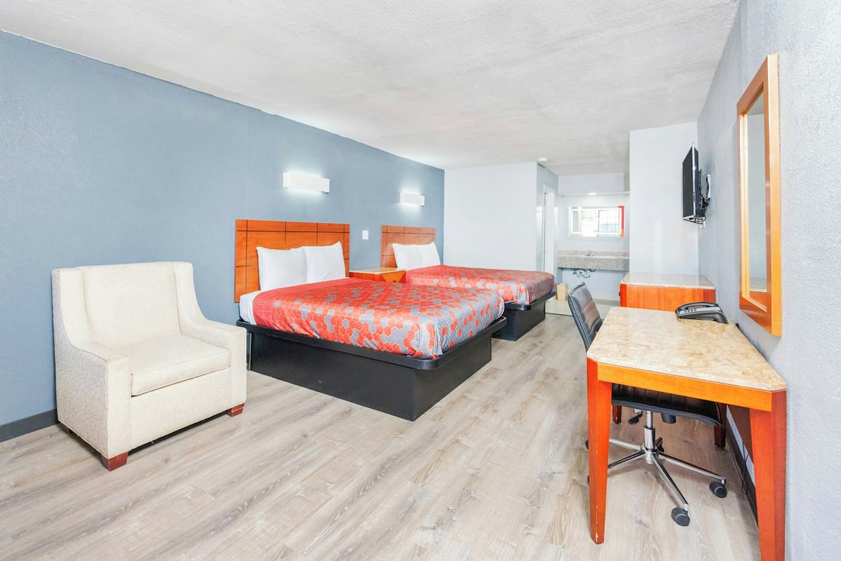 A hotel room with two beds, a desk, a chair, and a mirror.
