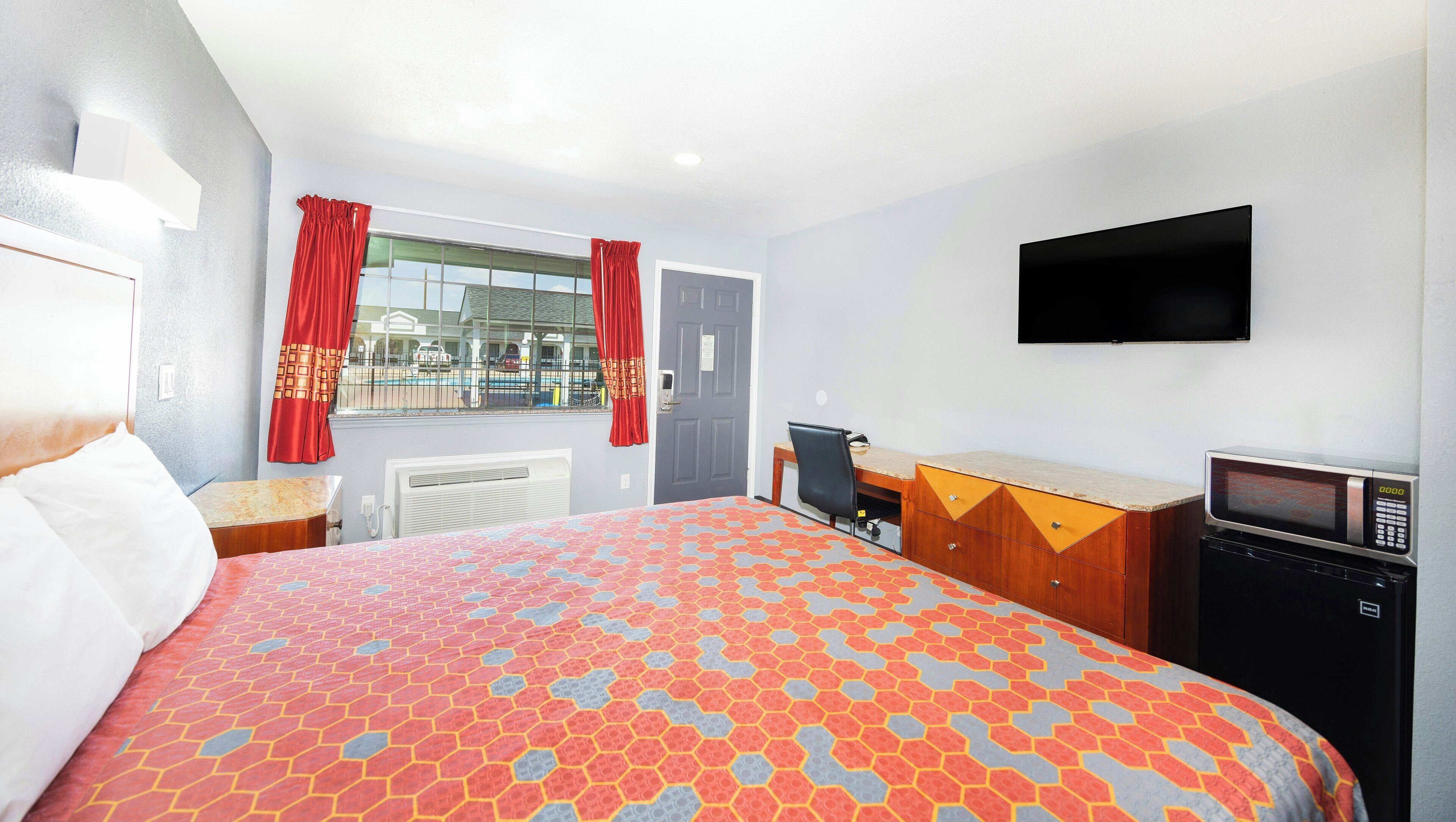 A hotel room with a bed, a desk, a TV, and a microwave.