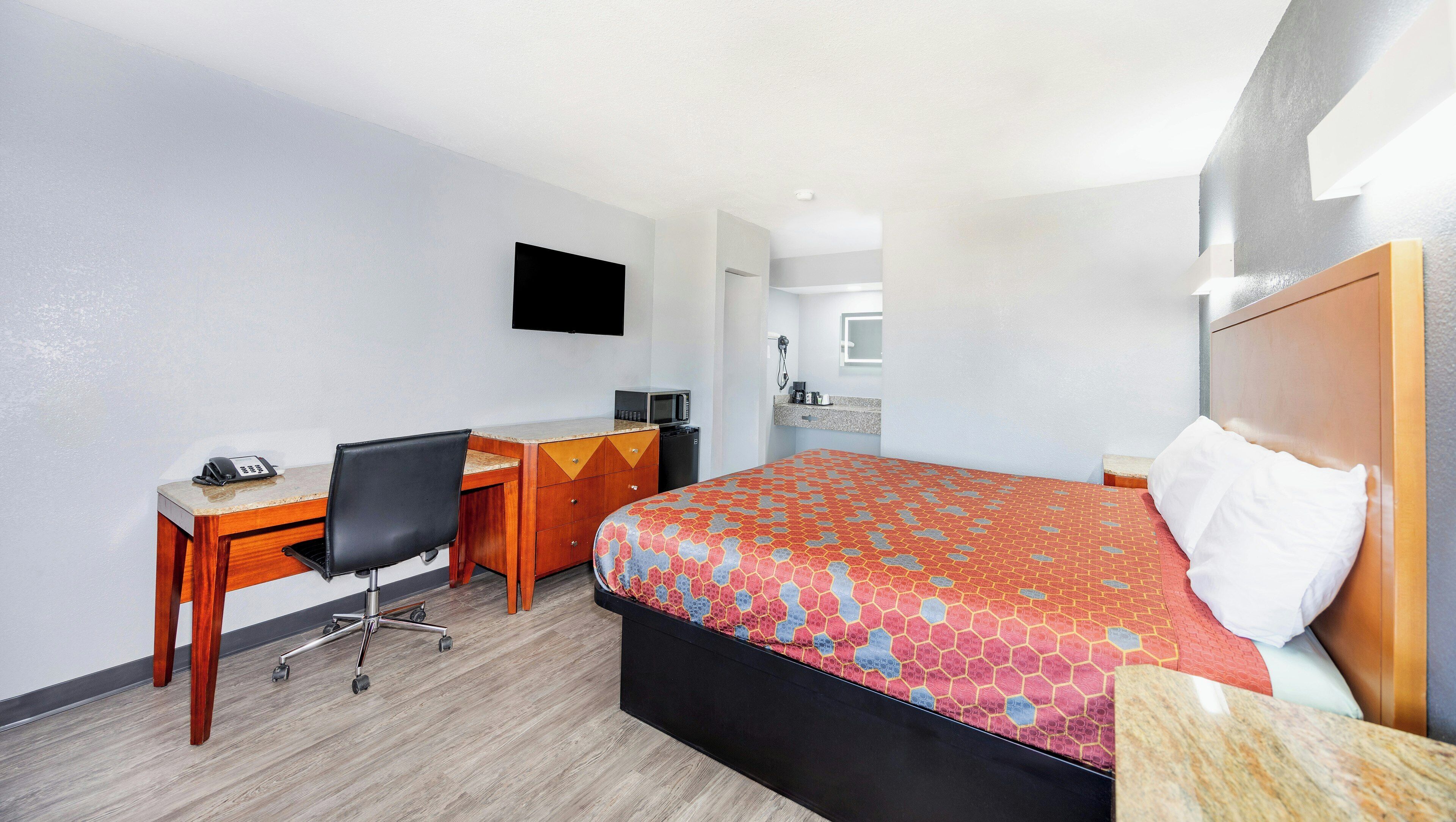 A hotel room with a bed, desk, chair, and a television on the wall.