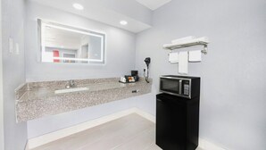 A modern bathroom with a granite countertop, a sink, a mirror, a hairdryer, a towel rack, and a microwave. - Executive Inn of Hondo (Hondo)