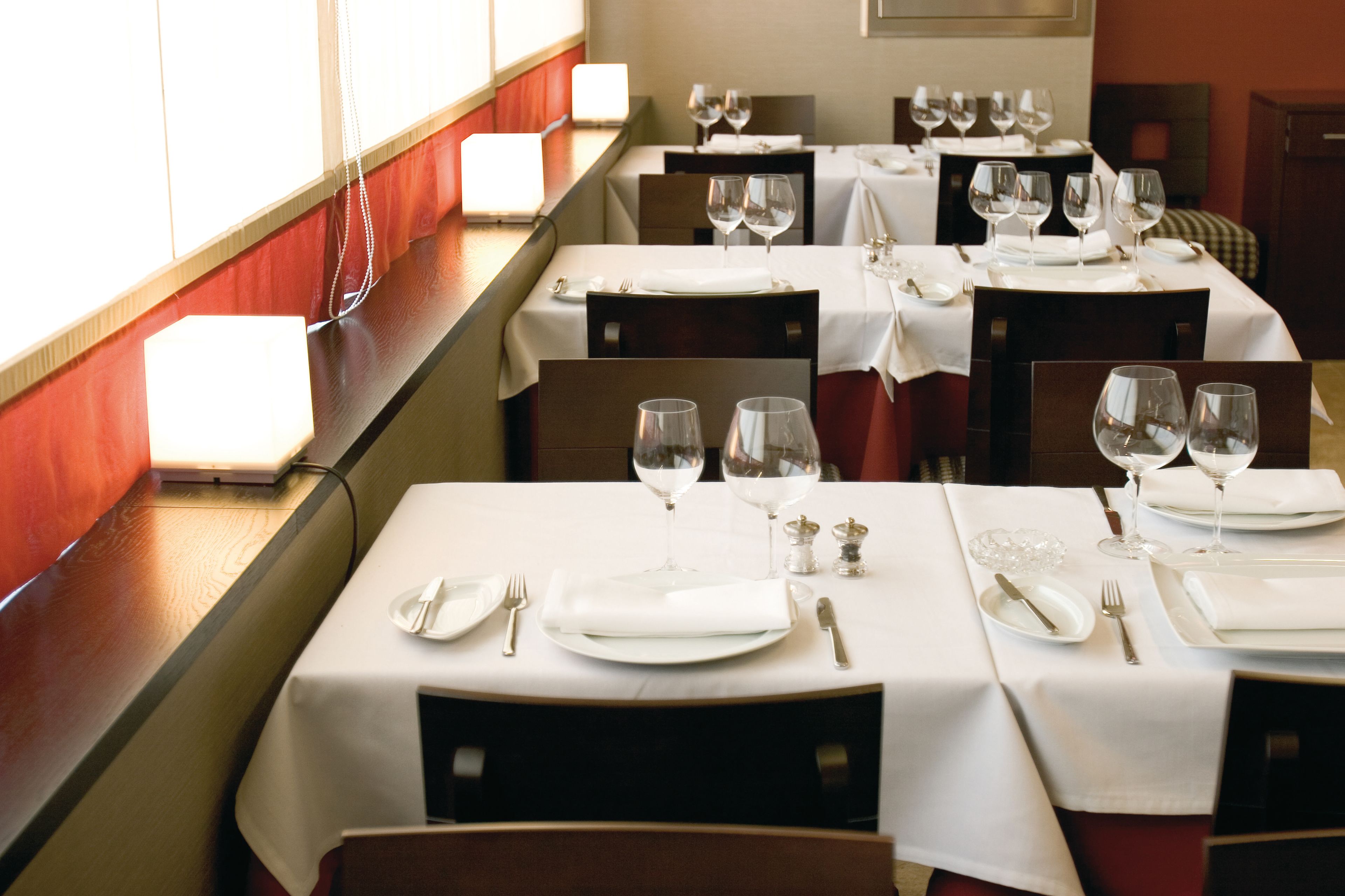 A restaurant with tables set for dining, featuring white tablecloths, wine glasses, and cutlery.