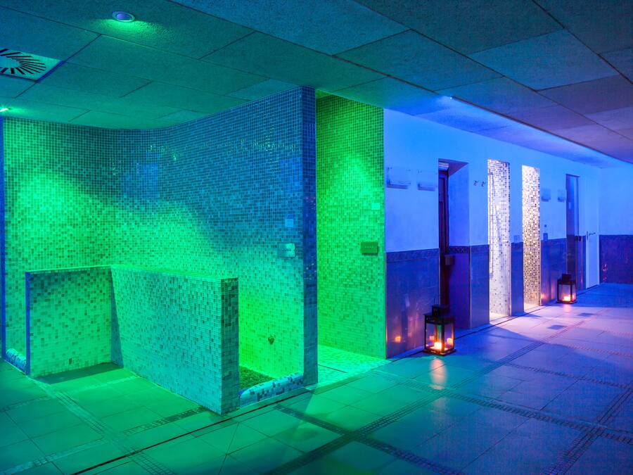 Un moderno espacio de spa con paredes y suelo de baldosas, iluminado con luces azules y verdes.