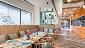 A restaurant with wooden tables and chairs, a teal-colored shelving unit, and a herringbone-patterned floor. - Occidental Aranjuez (Aranjuez)