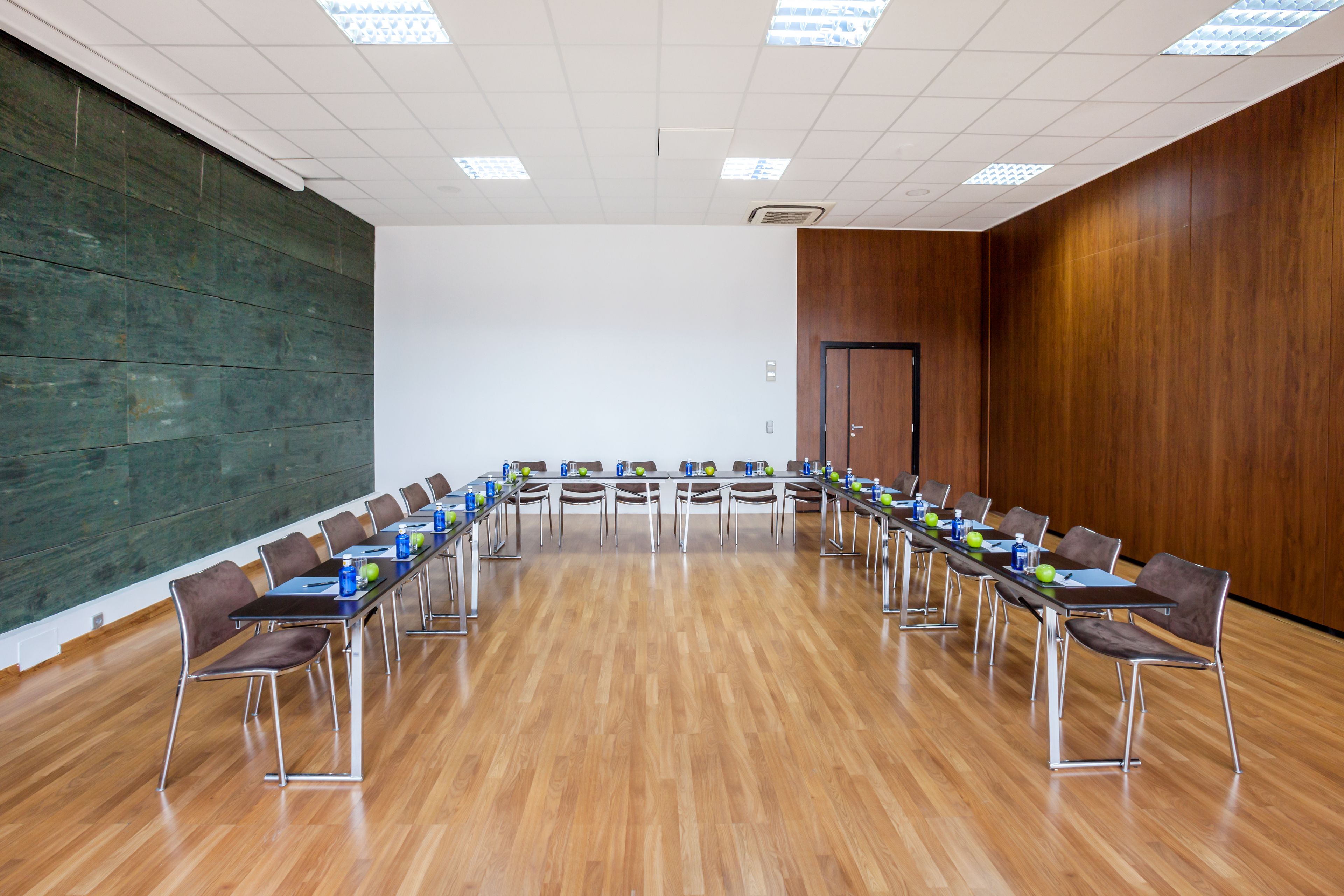 Un salón de conferencias con una larga mesa, sillas y una pared de madera.