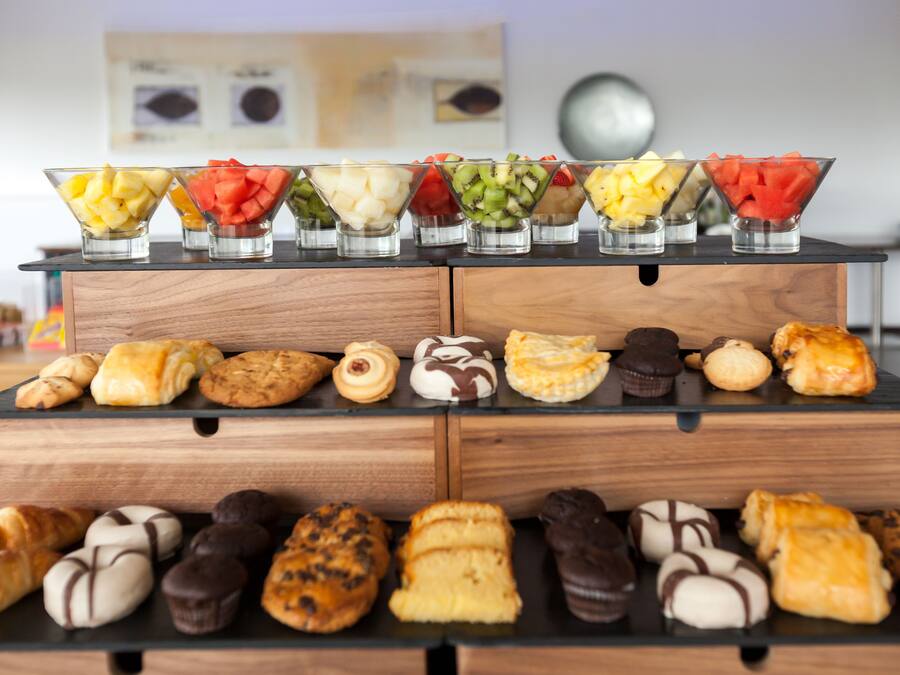 Una exhibición de pasteles variados y cuencos de fruta sobre una encimera de madera.