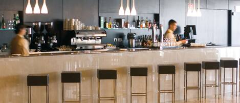 A modern bar with a polished marble countertop, multiple hanging pendant lights, and bar stools.