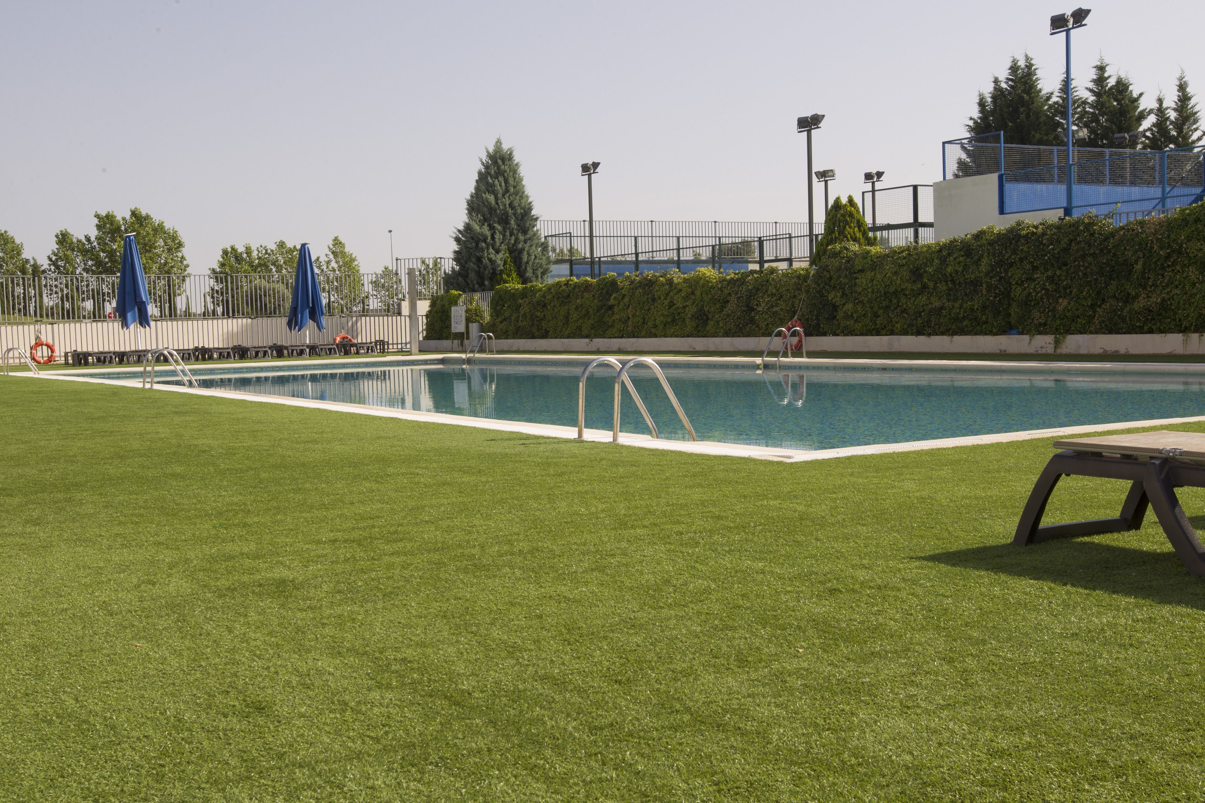 Une piscine avec une zone herbeuse devant, des échelles en métal et un poste de surveillance pour les sauveteurs.