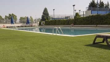 Una piscina con un área verde delantera, escaleras metálicas y un puesto de socorrista.