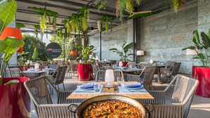 An outdoor dining area with wicker chairs, red planters, and a large pan of food on a table. - Occidental Aranjuez (Aranjuez)
