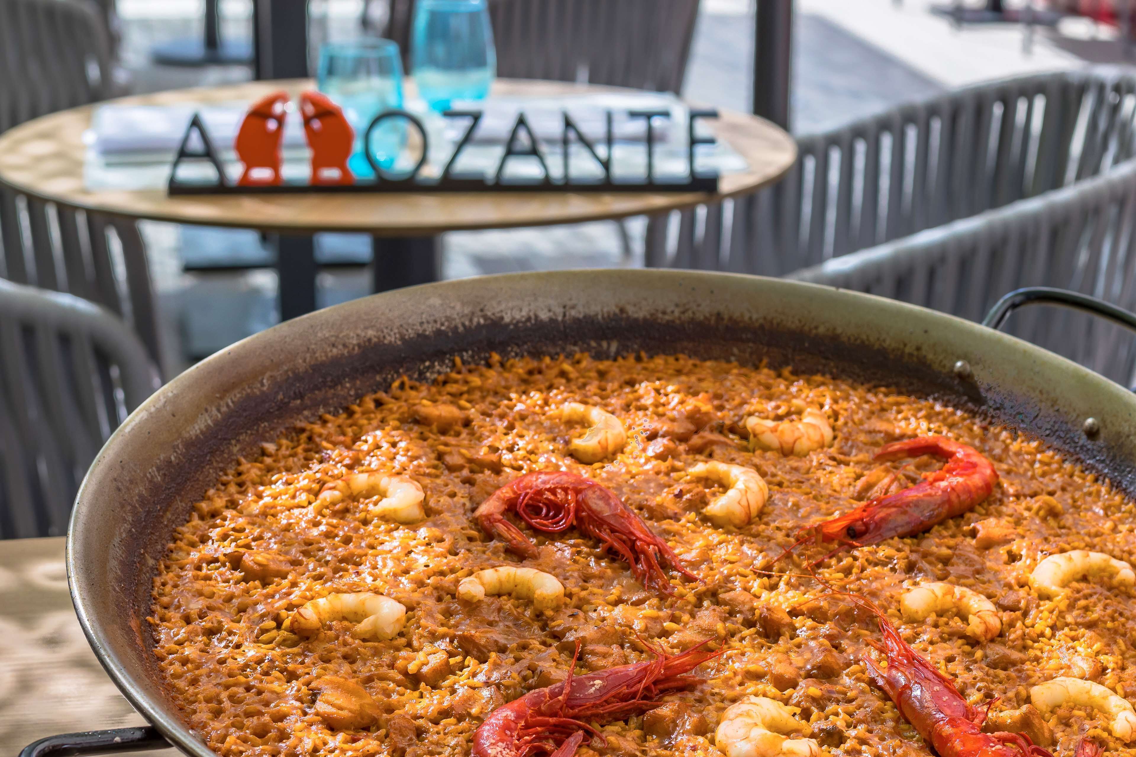 Una paellera grande de paella de mariscos con camarones y mejillones, sobre una mesa en un restaurante.