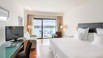 A hotel room with a bed, a desk with a TV, a chair, a small table, and a view of the outside.