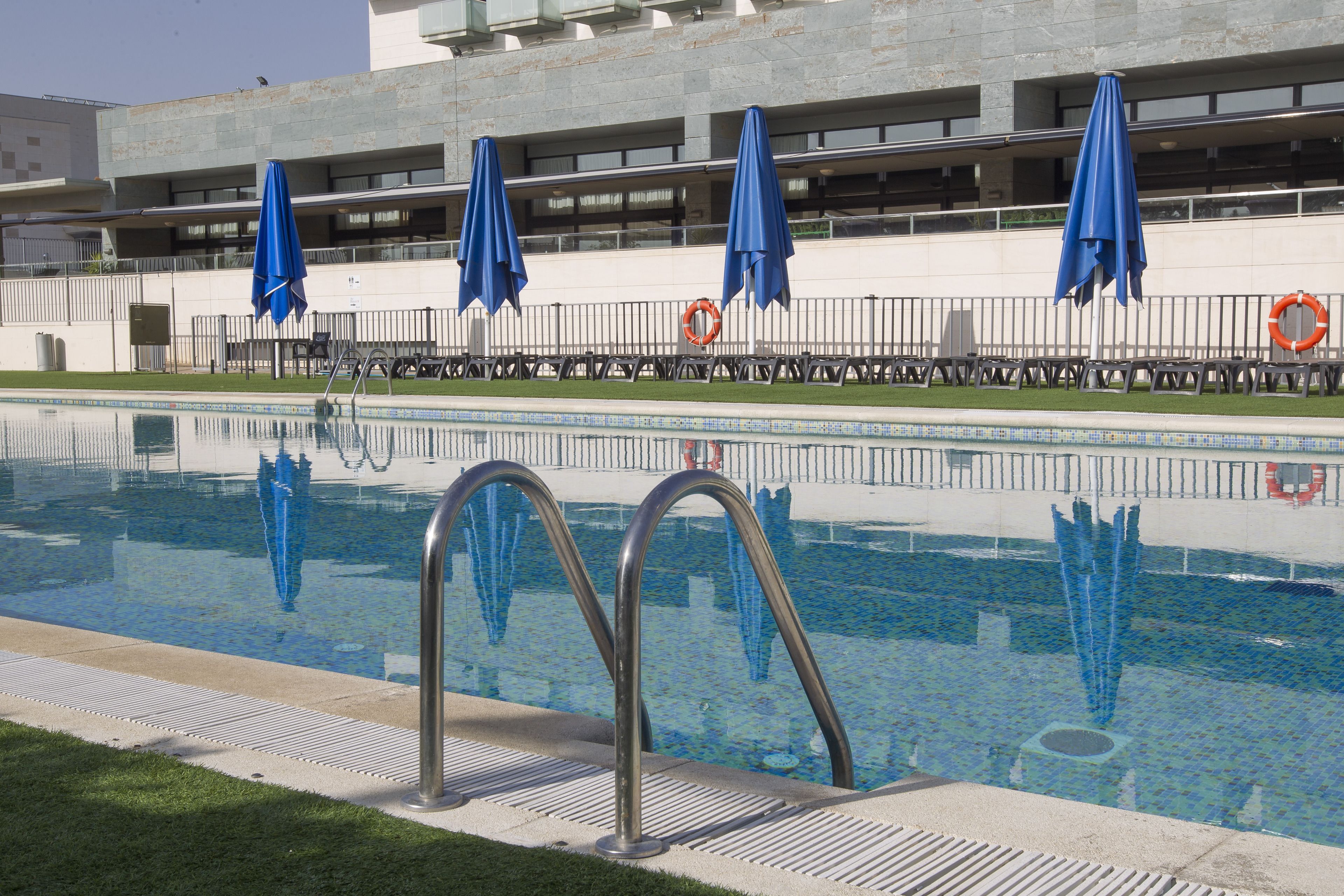 A swimming pool with metal ladders, blue umbrellas, and lifebuoys.