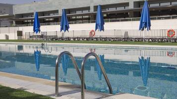 A swimming pool with metal ladders, blue umbrellas, and lifebuoys.