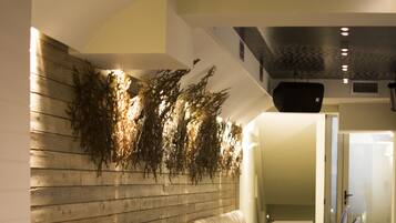 A restaurant with a long bench seating area, tables, and a wall with hanging greenery.