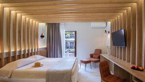 A modern hotel room with a bed, a desk, a TV, and a view of the outside balcony. - Bourtzi Hotel (Skiathos)