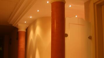 Un pasillo con una columna grande, una puerta y un muro con molduras decorativas.