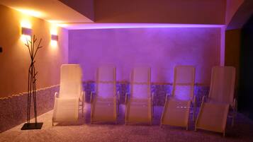 A spa area with six white lounge chairs arranged in a row, a stone wall, and a floor with a patterned tile design.