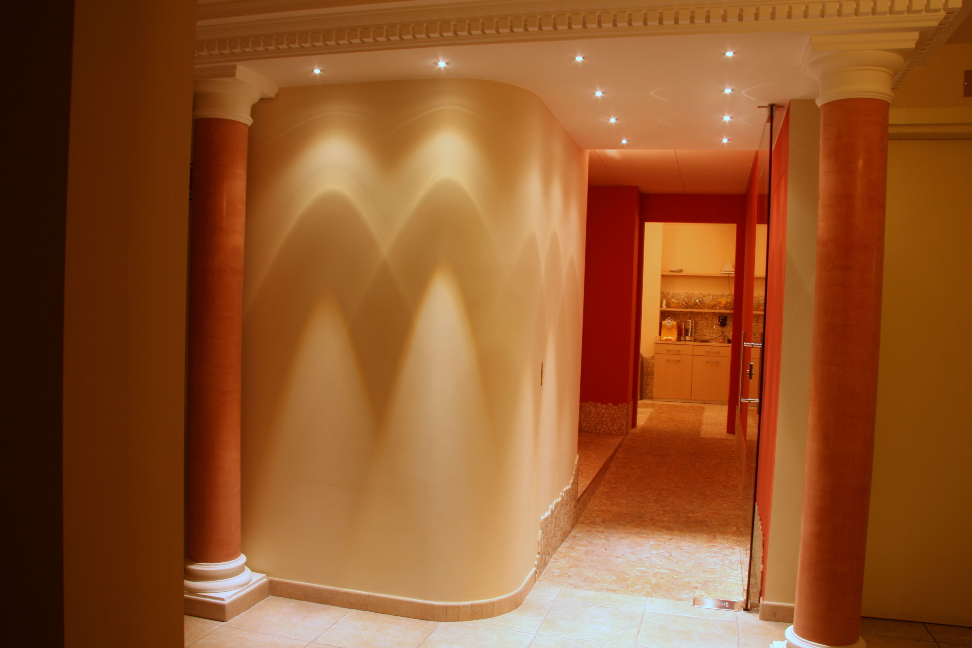 A corridor with columns, a curved wall, and a door leading to a room with a sink and cabinets.